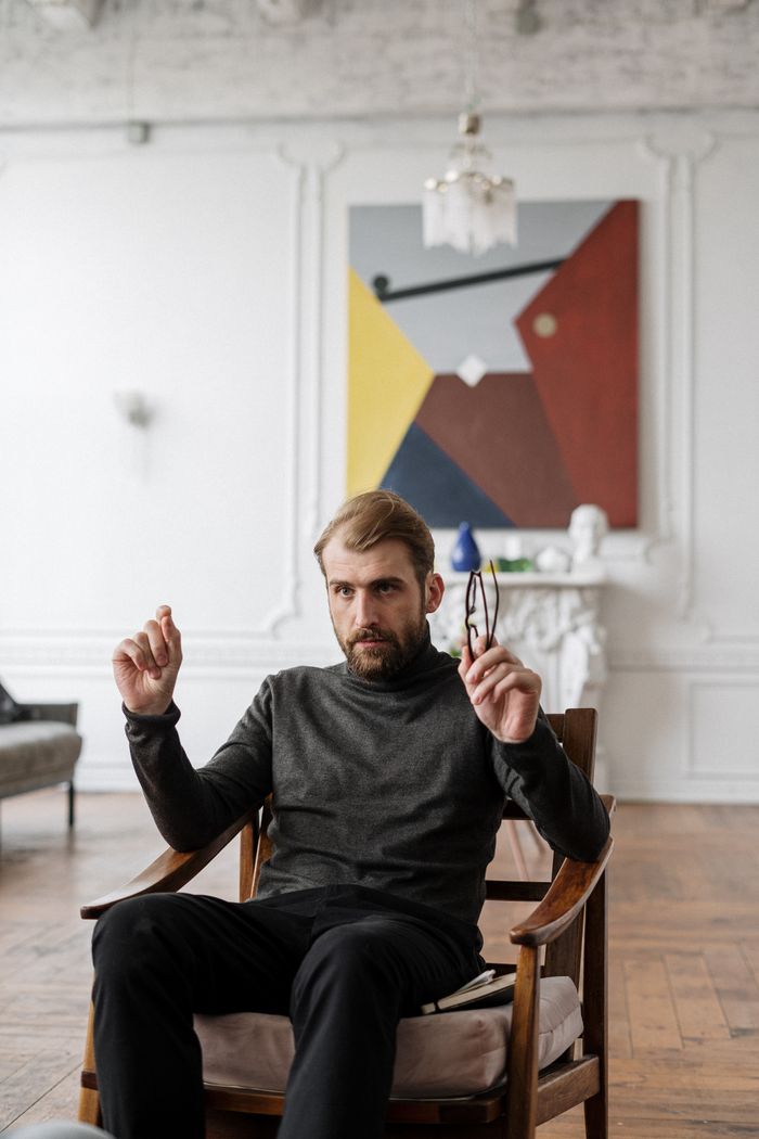hero-img-02 A man in a modern interior, sitting in front of an abstract painting, conveying thoughtful expression.