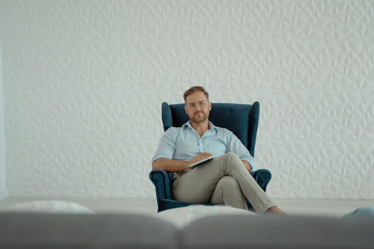 hero-img-01 A thoughtful man sitting cross-legged in an armchair against a stylish white background.